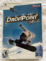 Front cover of Drop Point Alaska PC game box featuring snowboarder and helicopter.