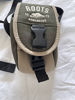 Front view of small Roots shoulder bag with flap displaying Roots Athletics logo and buckle closure.