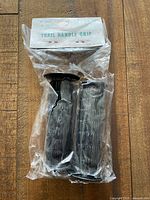 Vintage new old stock black rubber bike grips in torn plastic packaging with original labeled box on wood floor.