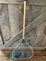 Full view of vintage fishing net showing wooden handle, green plastic triangular frame, and netting