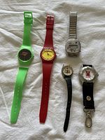Full view of all five watches laid out on fabric background, showing colors, styles, and sizes.