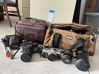 Overall lot showing two camera bags, two Olympus SLRs with lenses, extra lens in case, straps and caps