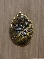 Front view of oval carved Tiger's Eye pendant set in 14k gold frame, showing flower carving detail.