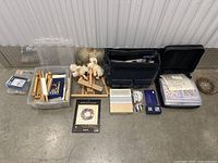 Overview photo of all lot items including wooden easel parts, sheep dolls, framed prints, canvases in plastic bins, and boxed art tools.