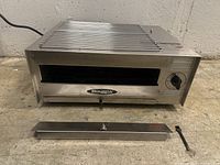 Full view of Biaggia pizza oven showing front with control knob, logo, crumb tray and handle removed and placed in front.