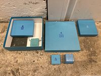 Four light blue Birks jewelry boxes displayed on floor, including two larger square boxes, a smaller box, and a small fabric pouch with Birks logo.