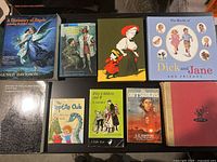 Photo showing 9 books arranged in 2 rows on a flat surface featuring various titles and illustrated covers.