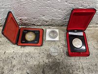 Four Canadian silver dollar coins in individual display cases, shown on a concrete surface.