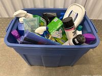 Blue storage bin filled with assorted cleaning supplies including spray bottles, aerosol cans, wipes, and sponges.