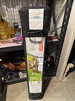 Black carry bag standing upright on metal shelving, showing front label with Coleman logo and product image.