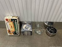 Full lot showing boxed Lagostina roasting pan, boxed HexClad pot, glass mixing bowl, and metal pot with strainer basket.