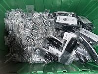 Large bin containing numerous coin cell batteries in plastic packaging along with several remote controls in plastic bags