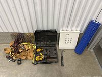 Photo showing cordless drill with black case, charger inside, hammer with black handle, white lockbox, and blue plastic organizer box.