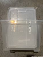 Top-down view of two square clear plastic storage containers stacked with lids visible, showing container bases and labels.