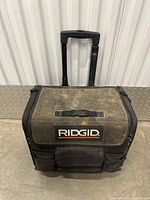 Black Rigid rolling tool bag with telescoping handle standing upright showing front and top sides.