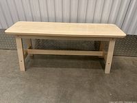 Light-color small wooden bench with flat rectangular seat, four legs, and horizontal support beam.