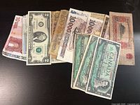 Photo of multiple foreign currency paper bills spread out on a dark surface.