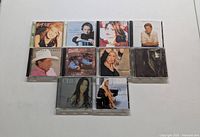 Photo of ten music CDs displayed in two rows on a white surface, featuring various artists and album artwork.