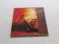 Front cover of the Eric Clapton Backless vinyl LP album showing Eric Clapton sitting on a couch with a guitar and lamp.