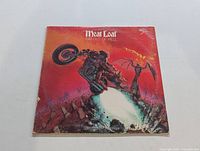 Front cover of Meat Loaf 'Bat Out of Hell' vinyl LP showing iconic artwork of a motorcyclist in a supernatural graveyard scene with red/orange background.