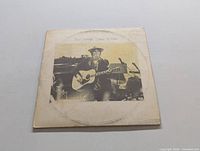 Front cover of the Comes a Time LP showing Neil Young playing acoustic guitar in sepia-tone photo on a white square background.