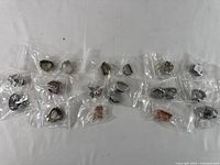 Overhead image of 19 individual Paparazzi costume rings, each bagged separately, showcasing variety in size, shape, and metal finish including silver and bronze tones, some with colored stones.