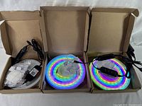 Three open boxes each containing a coiled neon LED tape kit with power cables, inline switch, mounting hardware and instructions.