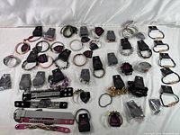 Wide shot showing over 45 Paparazzi bracelets laid out on a white surface, showcasing various styles including snap wraps, stretchy, cuffs, and beaded styles with tags attached.