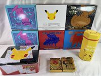 Seven empty Pokémon Elite Trainer Boxes from various sets stacked neatly with the Pikachu No. 025 yellow collector bag and two gold foil display cards arranged in front.