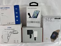Photo of five sealed electronic products including Wi-Fi camera, wireless mic, car phone holder, clip-on phone light, and smartwatch.