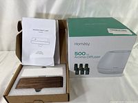 Wooden night lamp with manual and packaging alongside boxed Homasy aroma diffuser with essential oils shown on packaging.