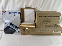 Lot showing all boxed items including the Nicewell digital food scale, V69 vacuum sealer, wooden night lamp, and portable searchlight.