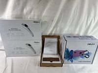 Two boxed Ice Cold IPL hair removal devices and the wooden magnetic night lamp with paperwork on white fabric background.
