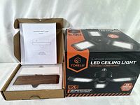 Photo showing the packaged wooden night lamp with instruction manual and the boxed Torelli 3-wing LED ceiling light.