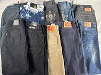 Top view of 10 stacked pairs of jeans showing various colors, styles, and Levi's branding on some.
