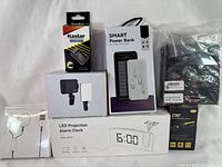 Photo showing seven items including rechargeable headlamp, power bank, LED projection alarm clock, fan and AA battery charger.