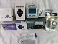 Full view of all nine boxed electronic items including smartwatch, wireless earbuds, phone telescope, digital timer, USB hub, aroma diffuser, magnetic charger, galaxy projector, and spy gadget.