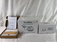 Photo showing all three boxed items: TinyBliss electric nasal aspirator, multifunctional magnetic LED wall lamp, and wooden night lamp with instructions.