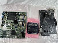 Overview of three vintage computer main boards including a large green Apple Mac Pro board, a smaller board with multiple memory modules, and a black Dell motherboard.