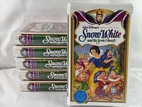 Photo showing six factory-sealed VHS tapes stacked horizontally with one tape standing upright to display front cover.