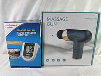 Photo showing Walgreens branded manual inflate blood pressure monitor box next to the packaged electronic massage gun massager box