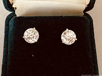 Front view of both stud earrings in open jewelry box on black velvet.