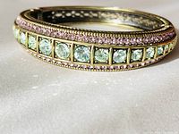 Close-up of bracelet showing large pale green rhinestones with small pink rhinestones above in a gold-tone metal setting.