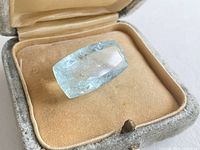 Aquamarine gemstone inside vintage jewelry box showing rectangular faceted cut and light blue color.