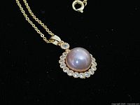 Close-up of pearl pendant encircled by halo of clear stones and part of gold chain