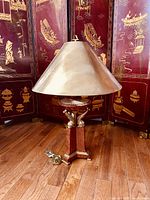 Full lamp showing gold metallic shade on wooden and brass dolphin-supported base