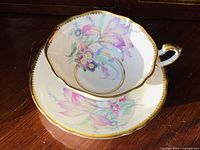 Teacup and saucer set showing delicate blush pink orchids and gold trim under natural light.
