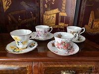 Four Royal Albert teacups and saucers arranged to show different floral patterns: yellow, pink, peach, and light brown flowers.