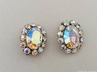 Front view of the pair of signed Sherman earrings with large oval AB rhinestone centers surrounded by smaller rhinestones, showing iridescent colors.