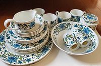 Full assortment of Staffordshire England Mid Winter dishware displayed grouped together, showing plates, bowls, cups, cream jug, salt and pepper shakers, and covered jar with floral pattern.